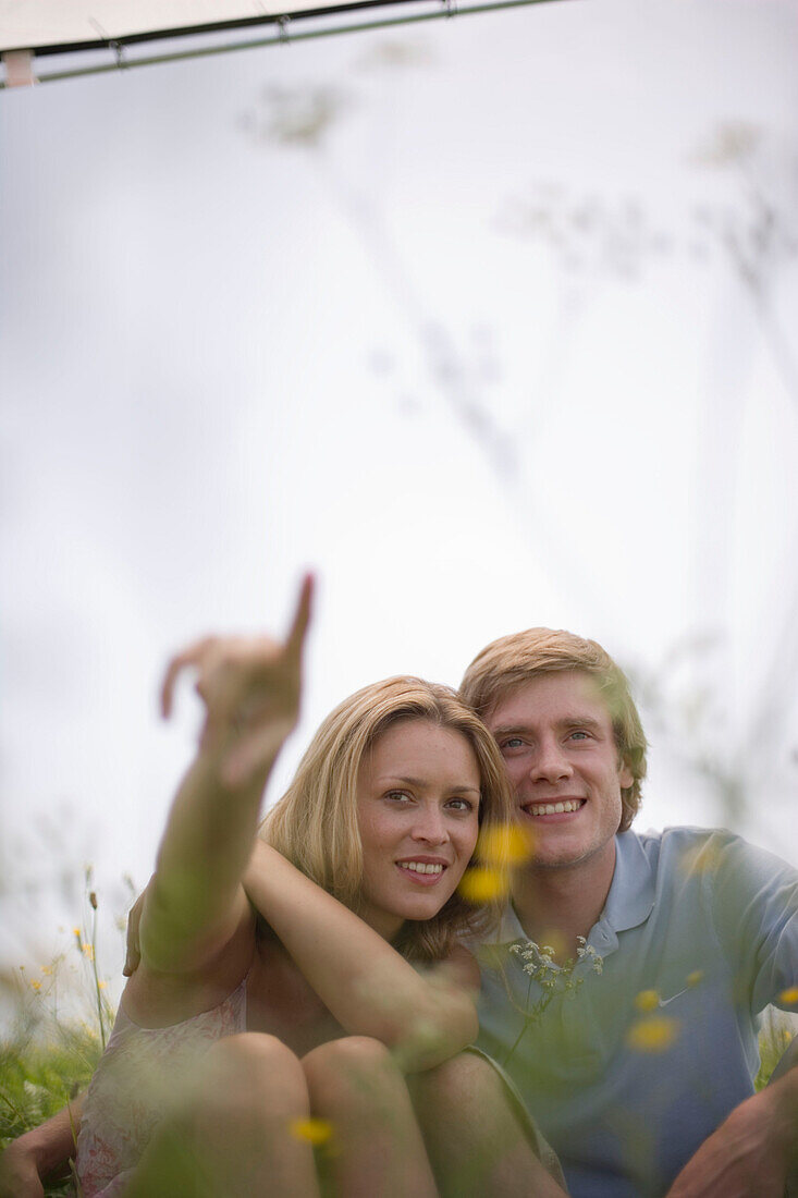 Young couple sitting on meadow, woman pointing