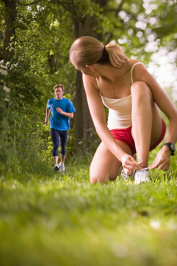 Female jogger tying lace, young man in Background