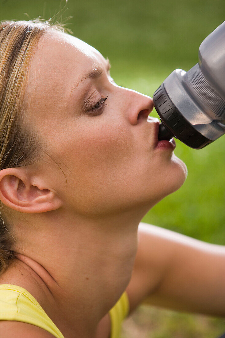 Woman resting while jogging, drinking from water bottle