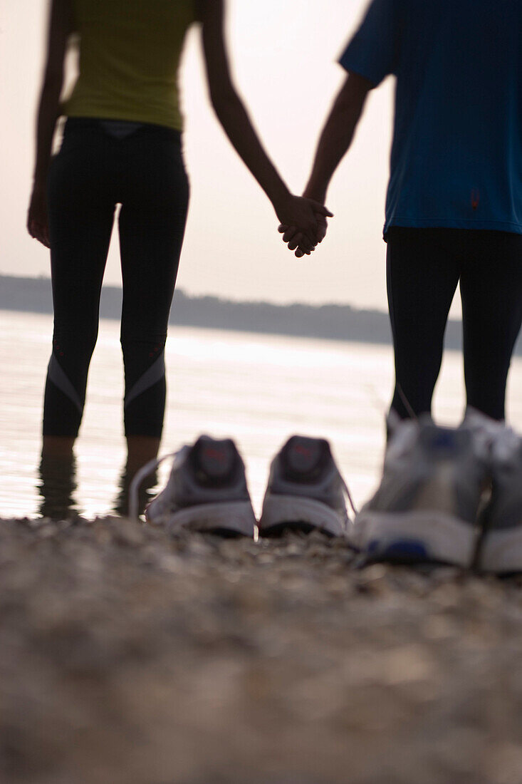 Couple standing (after jogging) on lakeshore, feet in water