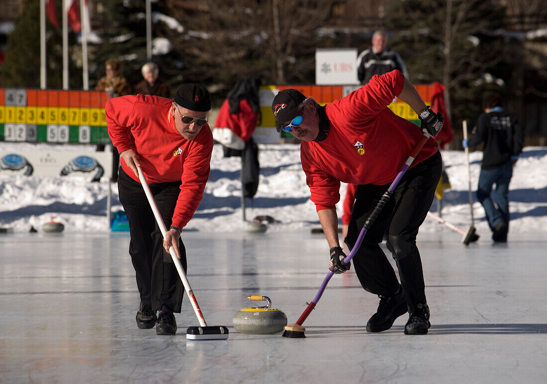 Two men curling on a rink, Zermatt, Valais, Switzerland (Curling: A rink game where round stones are propelled by hand on ice towards a tee (target) in the middle of a house (circle)).