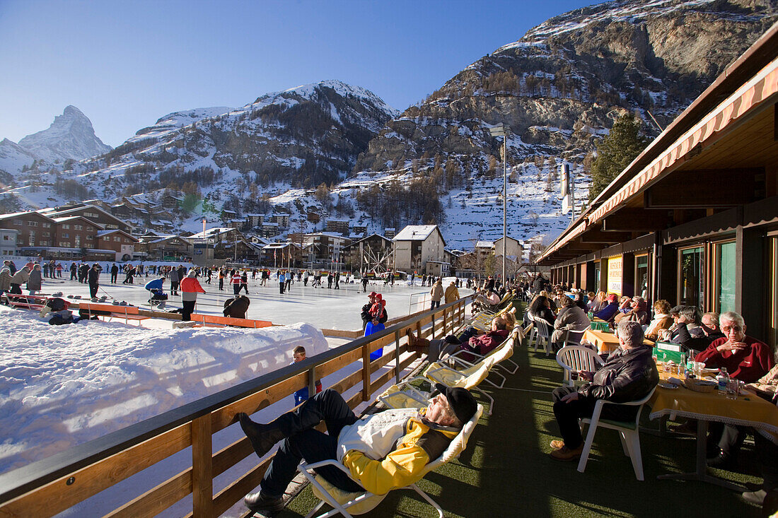 Visitors enjoying a curling game, Matterhorn in background, Zermatt, Valais, Switzerland (Curling: A rink game where round stones are propelled by hand on ice towards a tee (target) in the middle of a house (circle)).