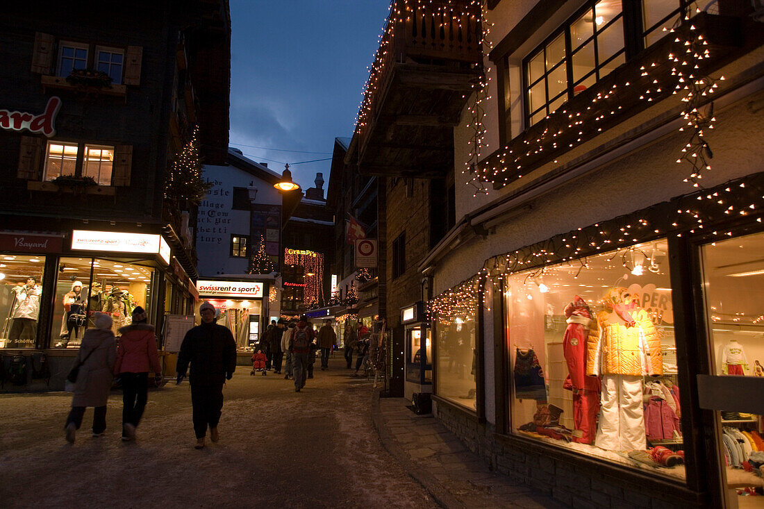 People walking over the illuminated shopping street Bahnhofstrasse in the late evening, Zermatt, Valais, Switzerland