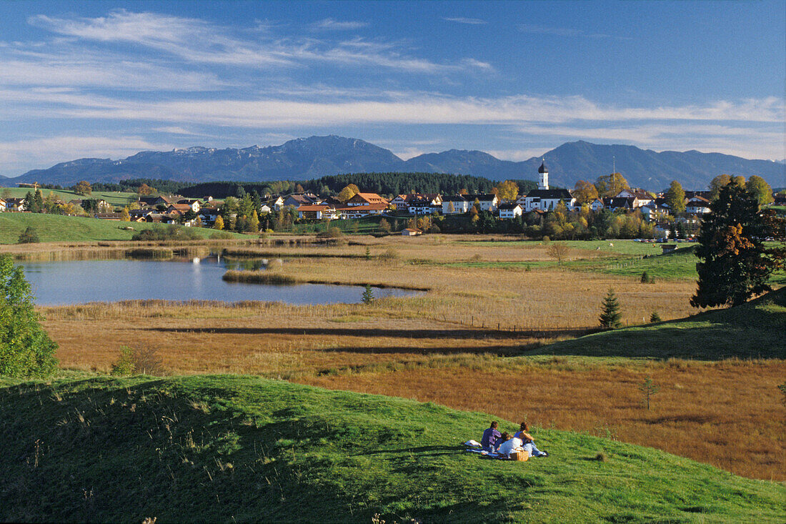 People having a picnic on hill looking onto Iffeldorf, Upper Bavaria, Germany