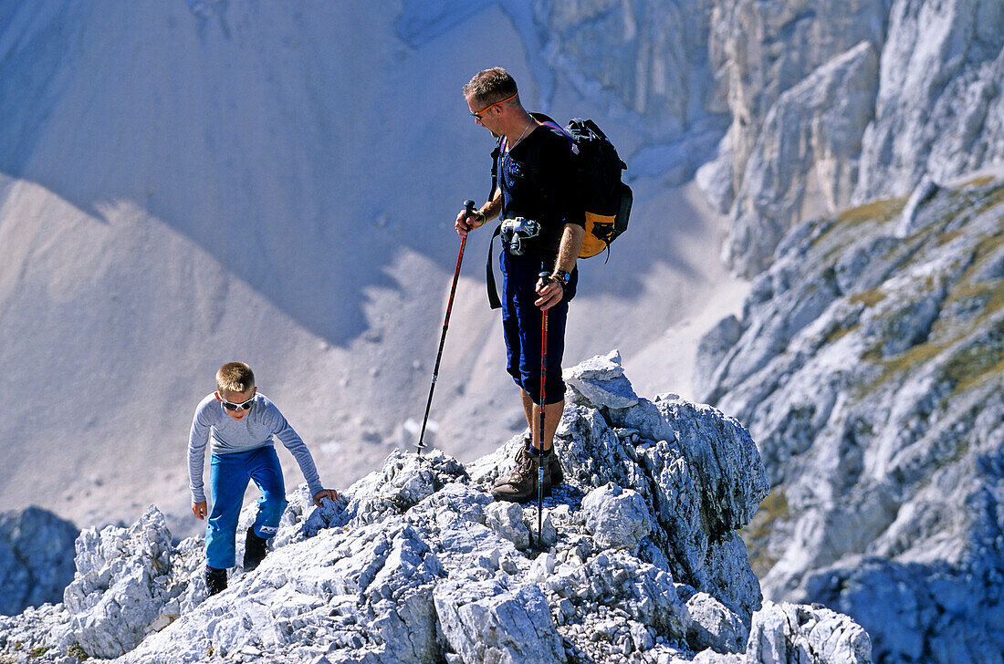 Father and son scrambling to the top of a rocky mountain. Summit of Amfiteater, Triglav Nationalpark, Julian Alps, Slovenia, Alps.