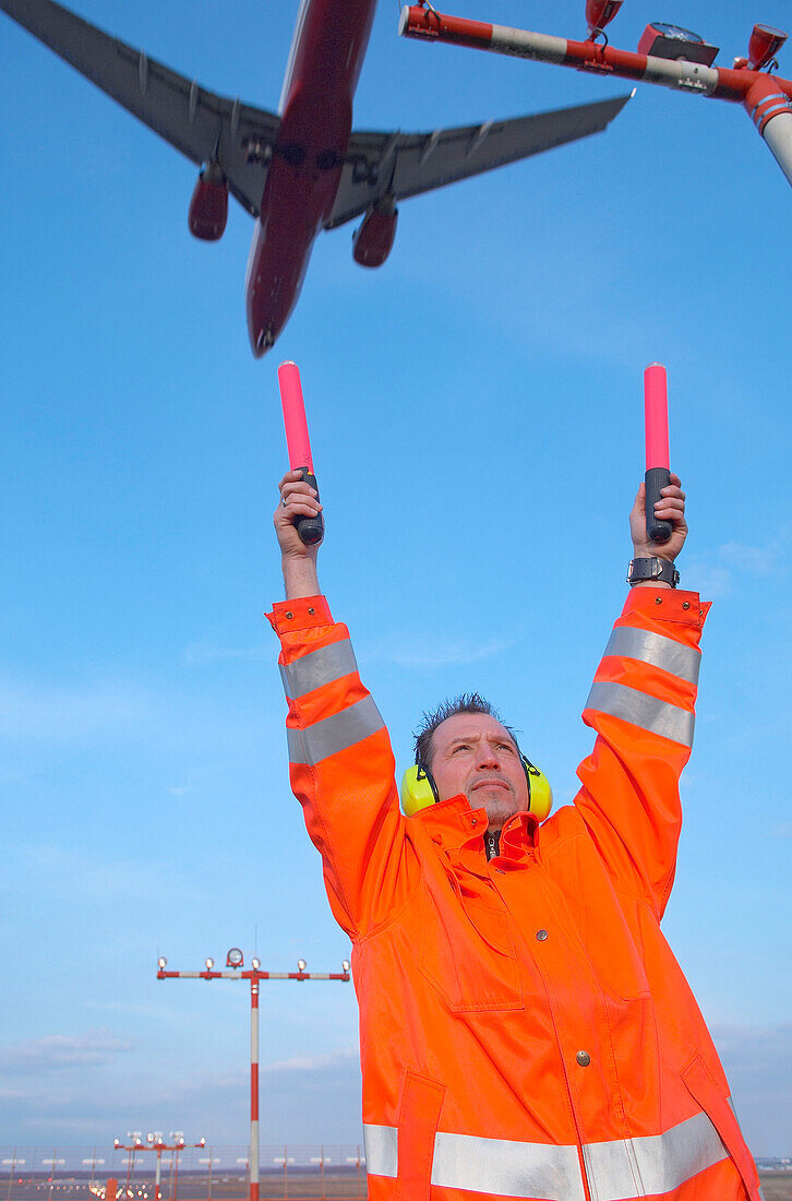 Airport ground crew holding up signaling sticks below approaching aircraft, Airport Düsseldorf, North Rine-Westphalia, Germany