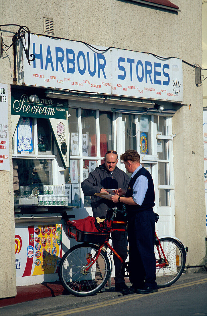 A postman delivering letters in front of a shop, Lyme Regis, Dorset, England