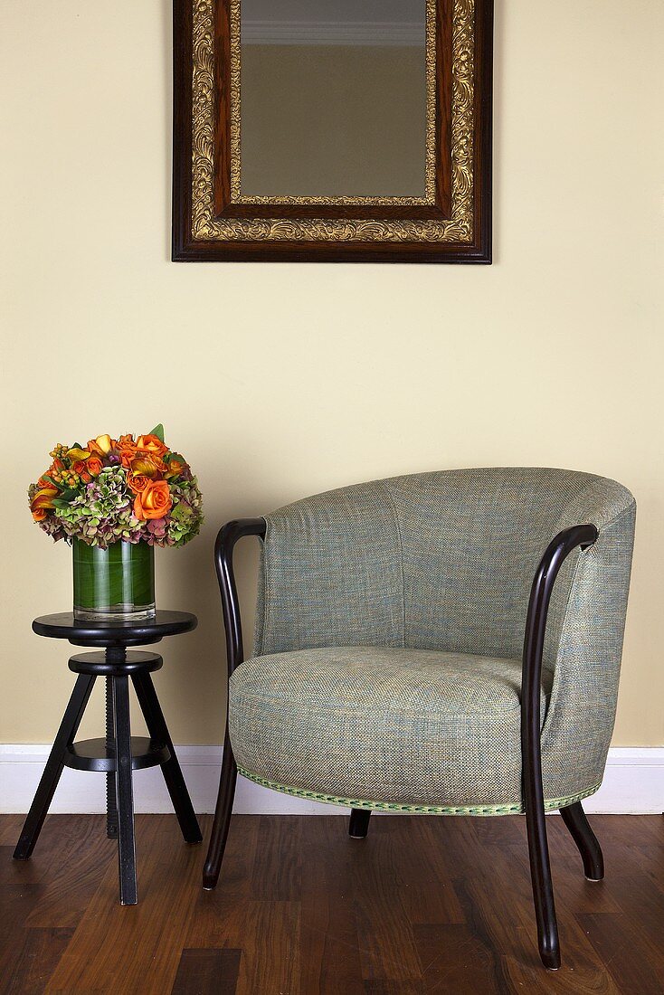 An upholstered armchair with a mottled grey cover and a black, height-adjustable side table in front of a pastel-coloured wall