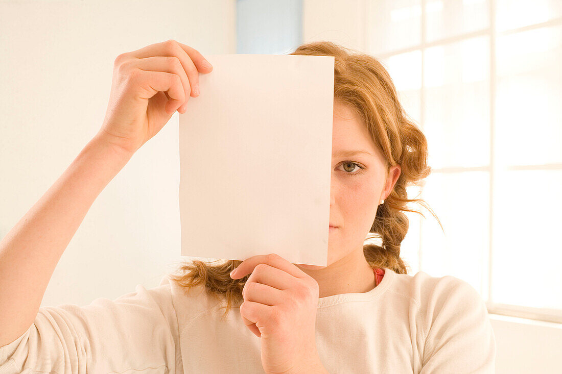 Teenage girl (14-16) holding sheet in front of face