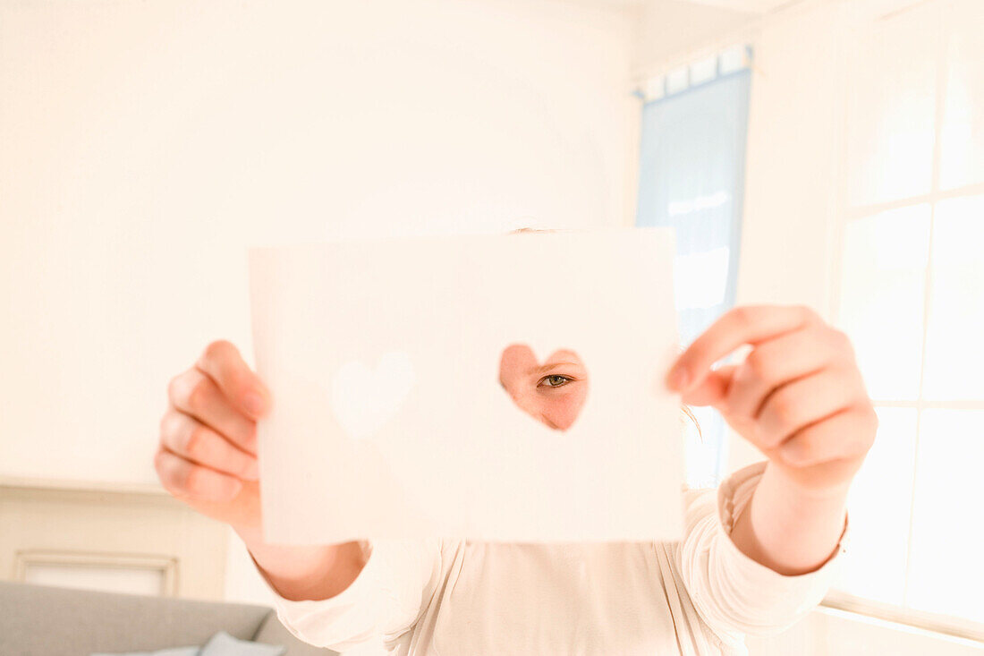 Teenage girl (14-16) holding sheet with hearts in front of face
