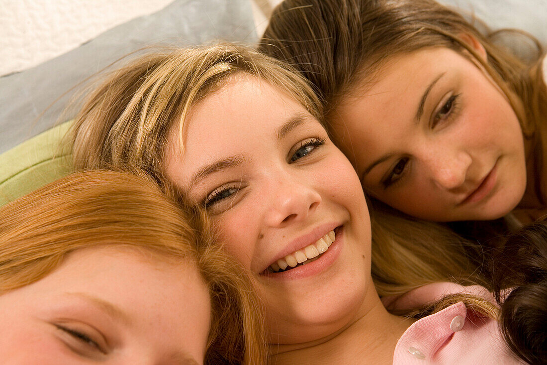 Three teenage girls (14-16) snuggling together on bed, close-up