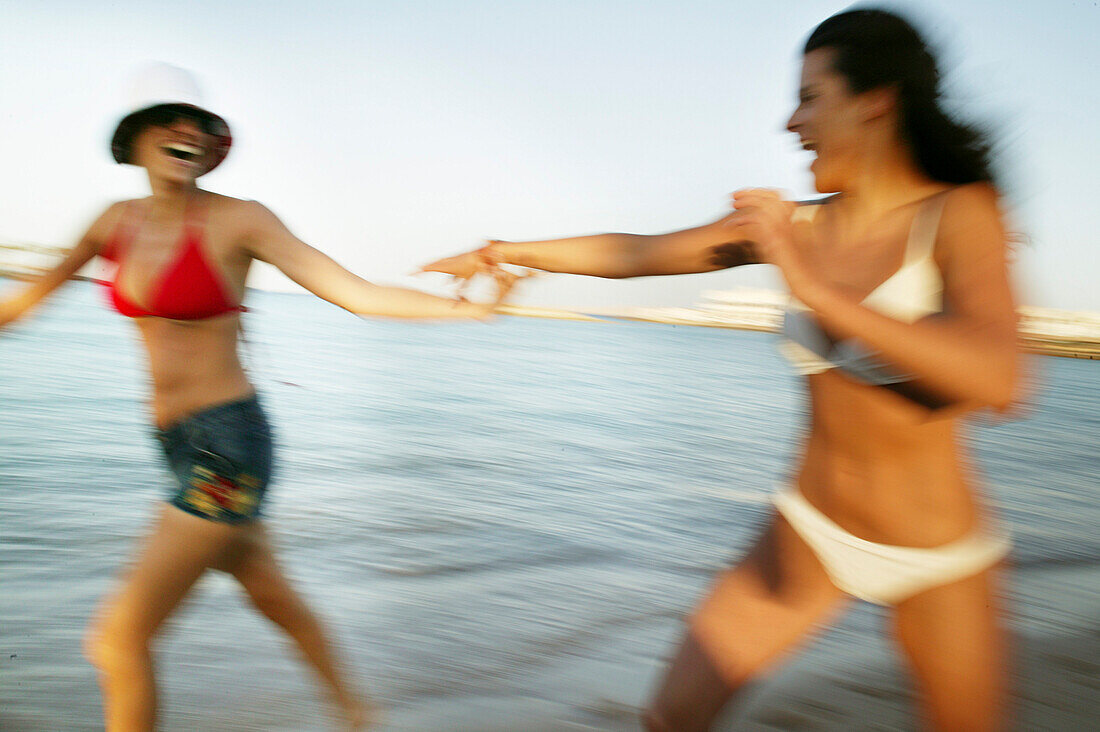 Two young women running on the beach, laughing, blurred motion