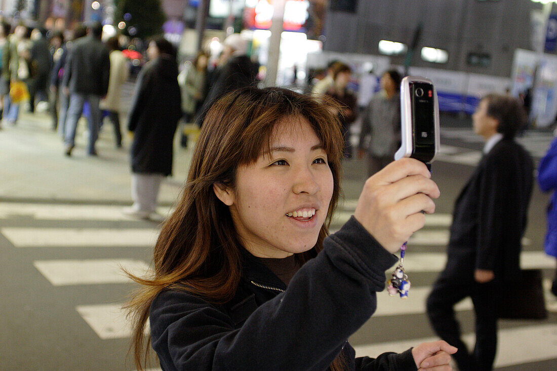 Young woman with cellular phone, mobil phone, at night, pedestrian crossing, East Shinjuku, Tokyo, Japan