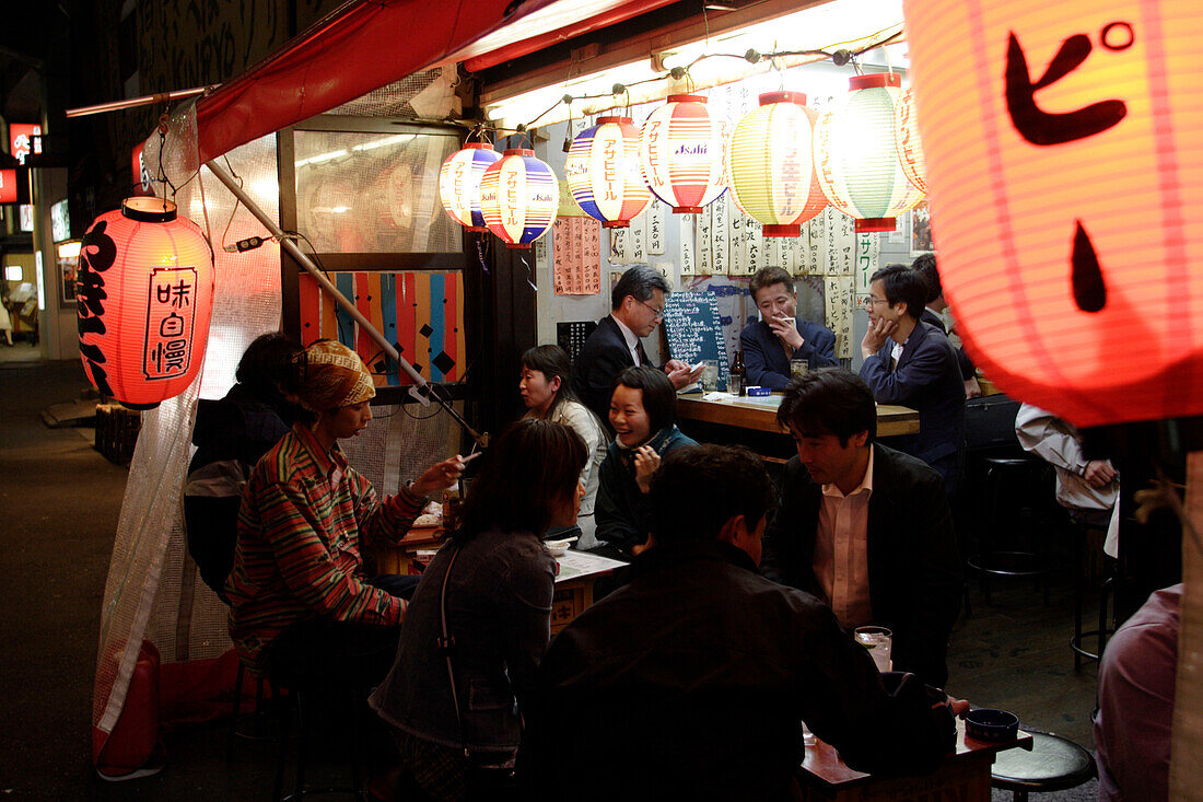 Menschen sitzen nachts vor einem Schnellimbiss, Yurakucho Yakitori Alley, Ginza, Tokio, Japan