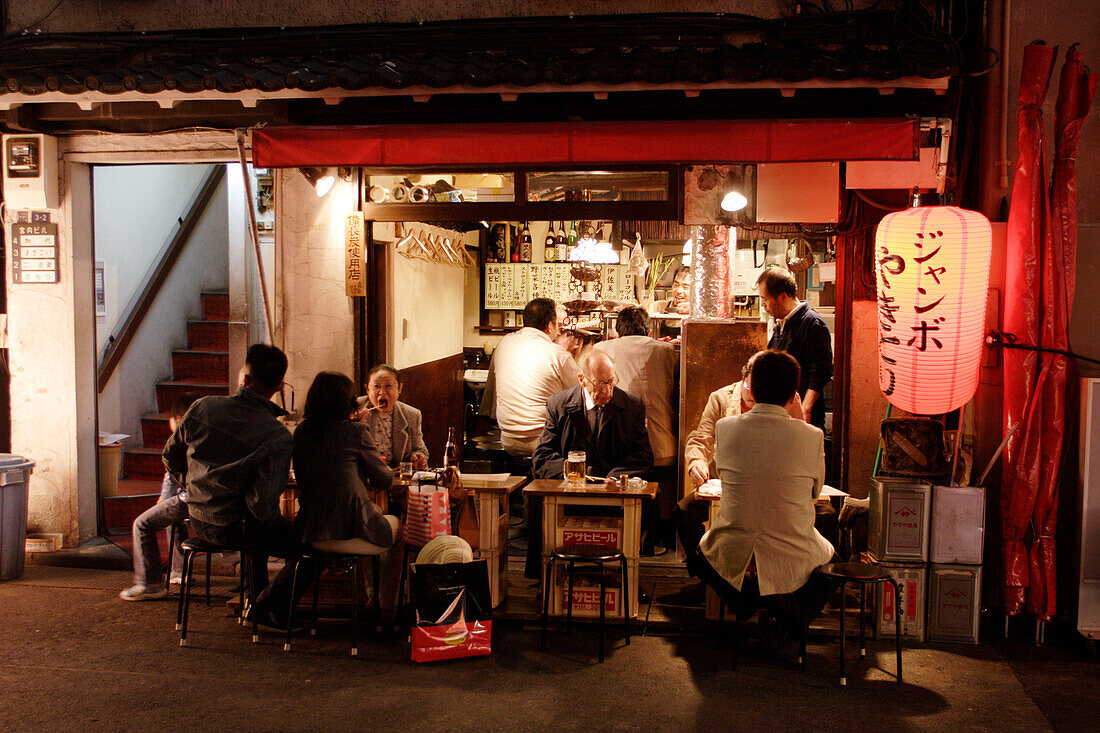 Menschen sitzen nachts vor einem Schnellimbiss, Yurakucho Yakitori Alley, Ginza, Tokio, Japan