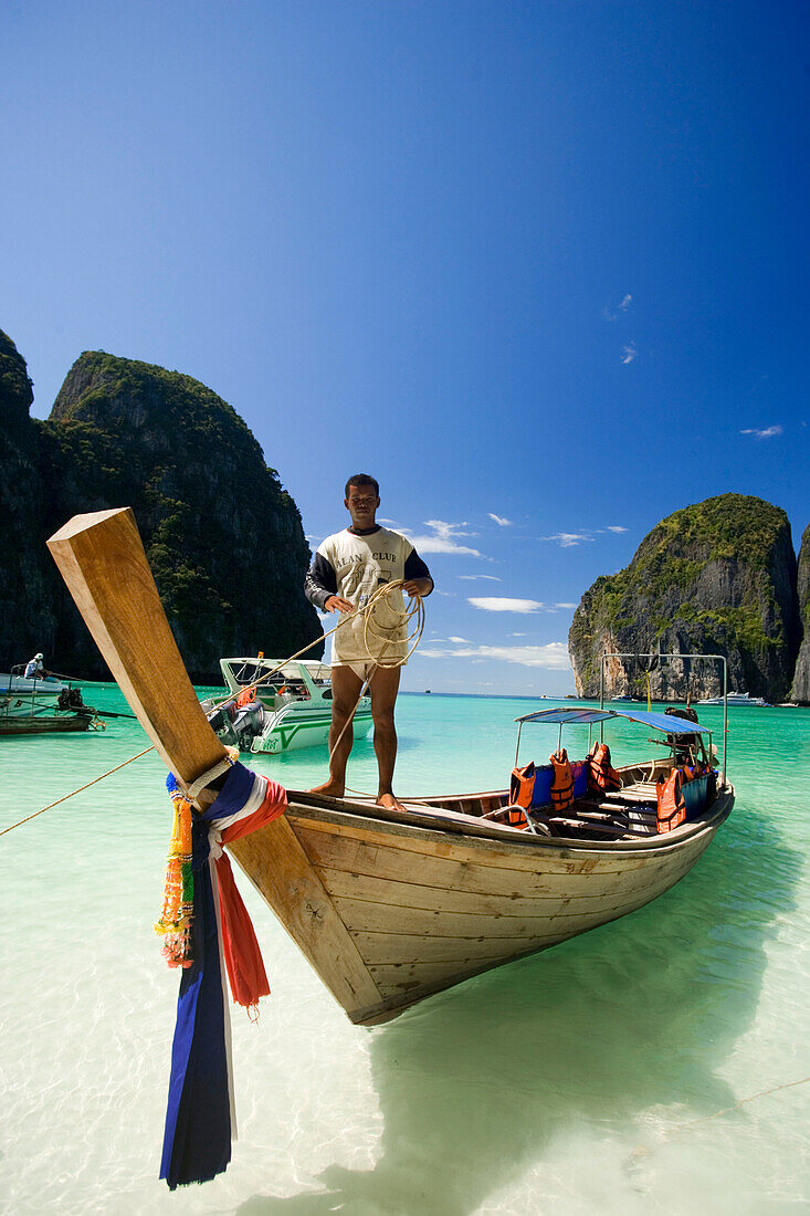 Boatman standing on a long tail boat and holding a rope, Maya Bay, a beautiful scenic lagoon, famous for the Hollywood film "The Beach", Ko Phi-Phi Leh, Ko Phi-Phi Islands, Krabi, Thailand, after the tsunami