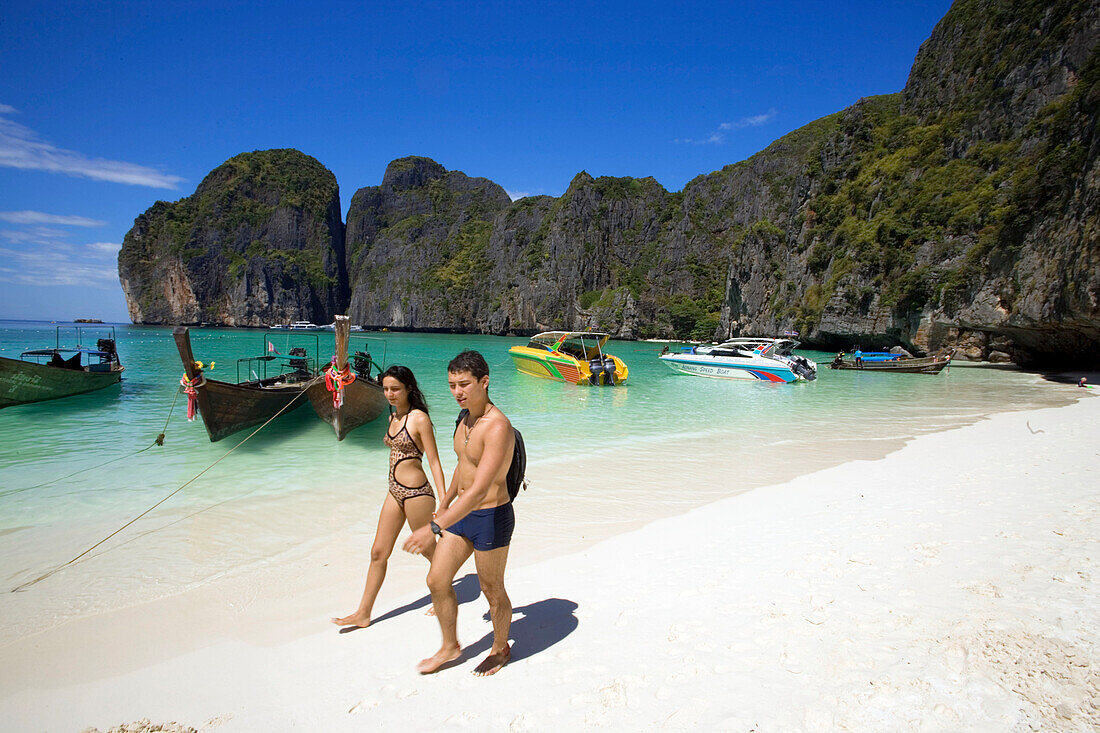 A young couple walking over the beach, anchored boats in background, Maya Bay, a beautiful scenic lagoon, famous for the Hollywood film "The Beach", Ko Phi-Phi Leh, Ko Phi-Phi Islands, Krabi, Thailand, after the tsunami