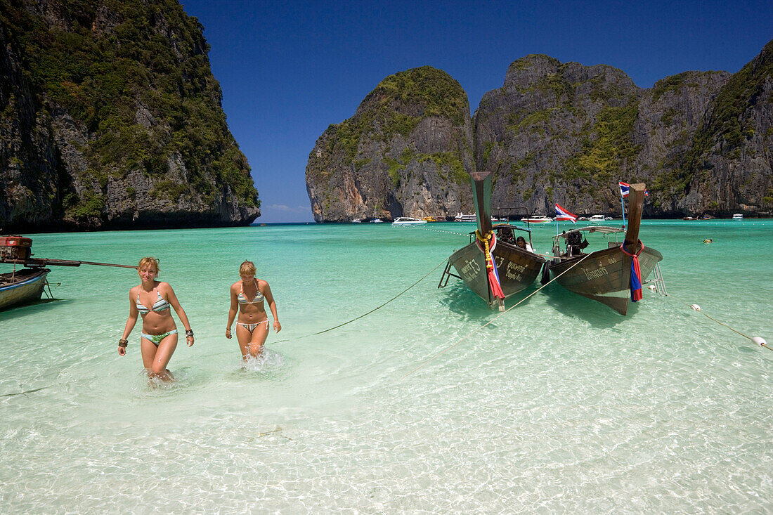 Two young women wearing bikini walking through shallow water, Maya Bay, a beautiful scenic lagoon, famous for the Hollywood film "The Beach", Ko Phi-Phi Leh, Ko Phi-Phi Islands, Krabi, Thailand, after the tsunami