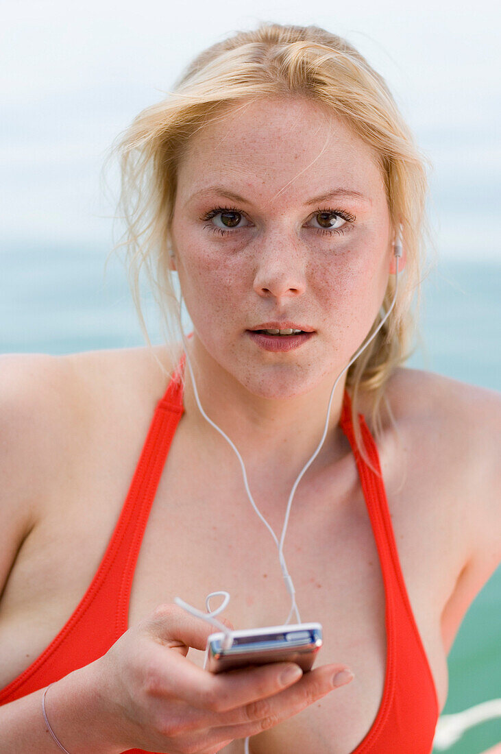 Young woman wearing red bikini, listening to portable MP3 player, Starnberger See, Upper Bavaria, Germany