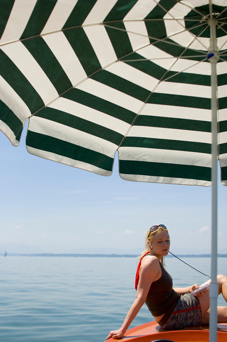 Woman sitting on rental boat with sunshade, listening to MP3 player, Starnberger See, Upper Bavaria, Germany