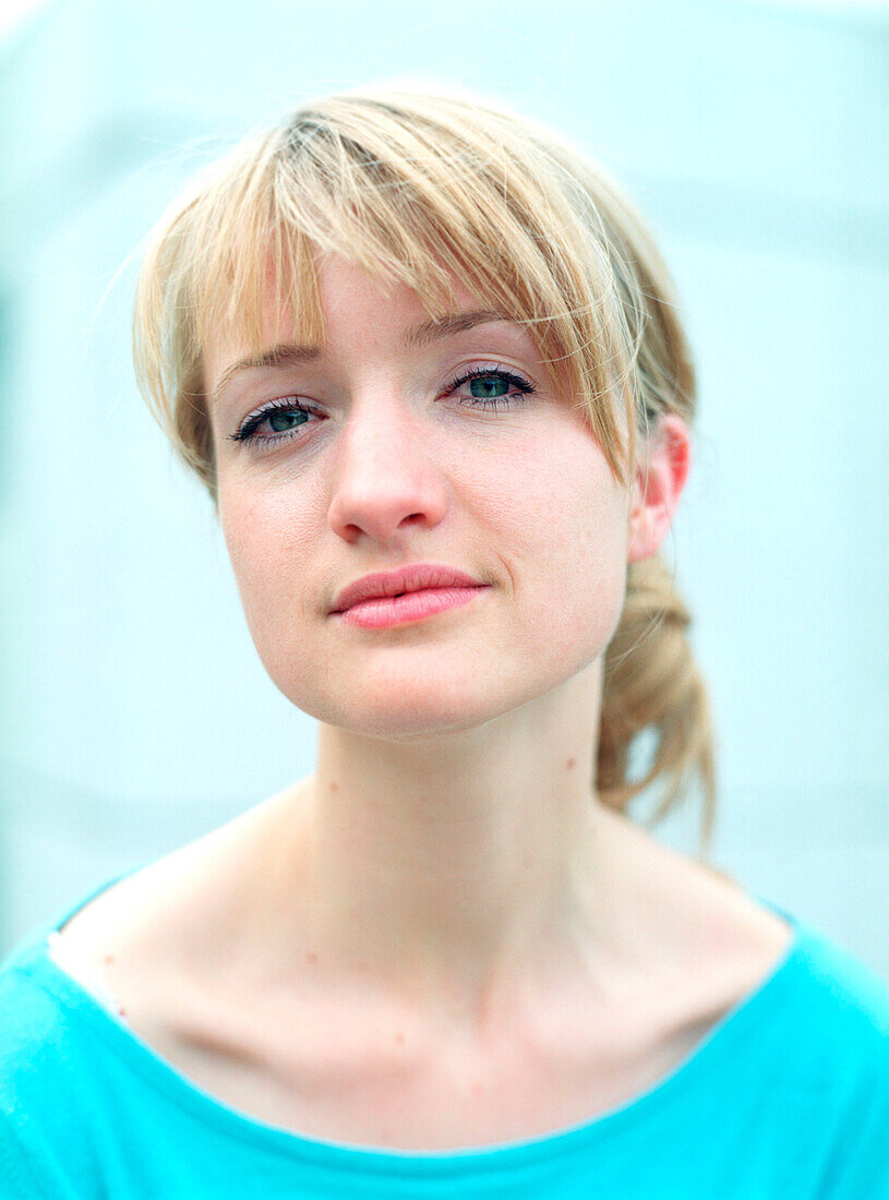 Portrait einer jungen blonden Frau mit türkisem Hemd