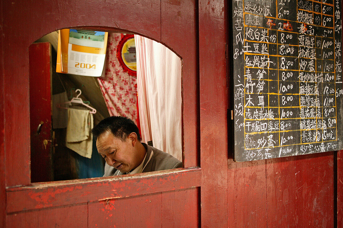 Mann sitzt in einer Kabine neben Speisekarte, Kantine des Kloster Xixiang Chi, Emei Shan, Provinz Sichuan, China, Asien