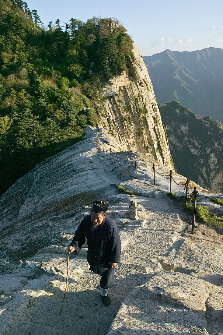 daoist monk on Fish Back Ridge, approaching Cui Yun Gong Monastery on South Peak, pilgrim path along stone steps with chain handrail,  cliffs of West Peak, Hua Shan, Shaanxi province, Taoist mountain, China, Asia