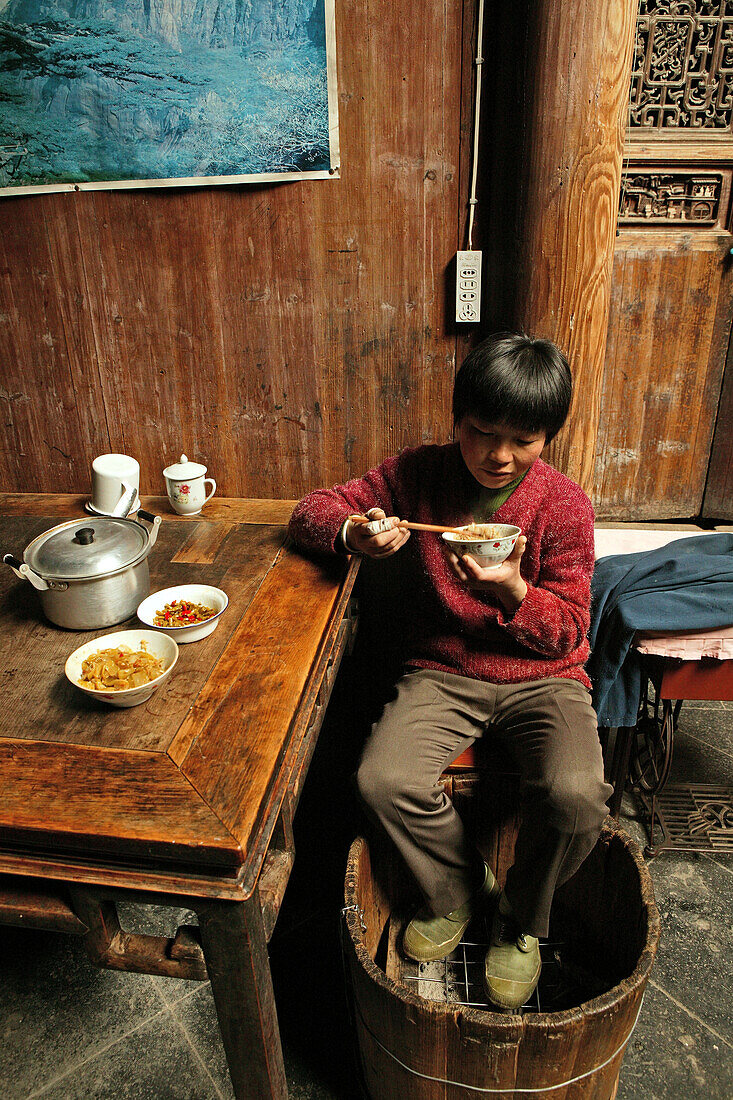 Ein Junge wärmt sich beim Essen an einem Fusswärmer Huo Tong, Hongcun, Huang Shan, China, Asien