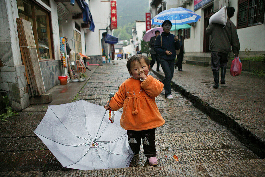 Kleines Mädchen mit Schirm in einer Gasse im Dorf Jiuhuashan, Provinz Anhui, China, Asien