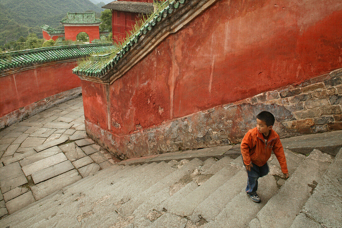 Child climbing the steps, red walls of the Purple Cloud Temple, Zi Xiao Gong, Mount Wudang, Wudang Shan, Taoist mountain, Hubei province, UNESCO world cultural heritage site, birthplace of Tai chi, China