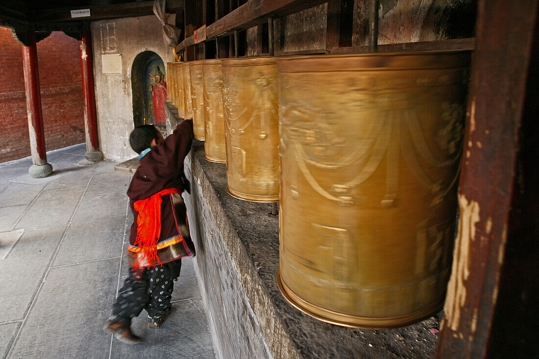 Child monk turning the prayer wheels at the base of the Great White Pagoda during the birthday celebrations for Wenshu, Tayuan Monastery, Wutai Shan, Five Terrace Mountain, Buddhist Centre, town of Taihuai, Shanxi province, China