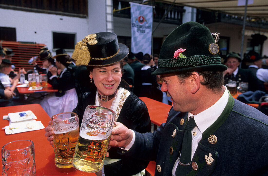 young couple in dirndl dress and traditional dress, saying cheers in beer garden, pilgrimage to Raiten, Schleching, Chiemgau, Upper Bavaria, Bavaria, Germany