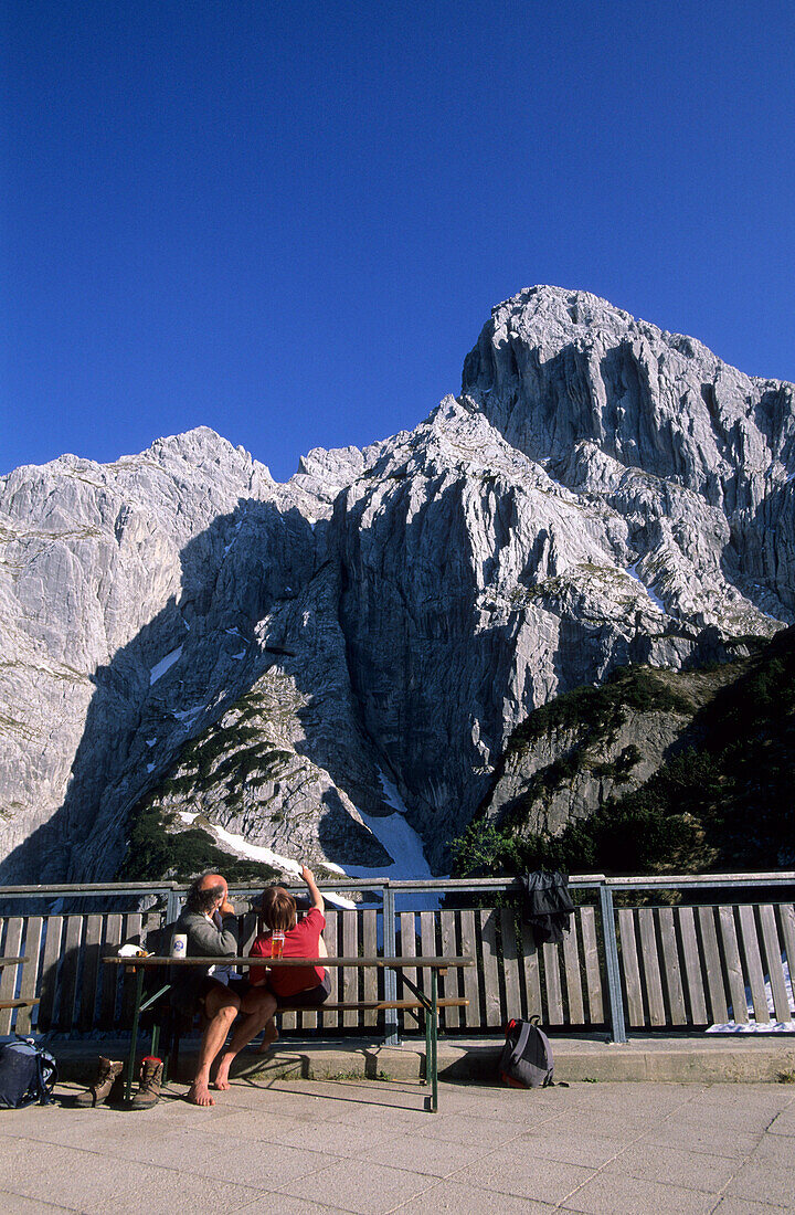 terrace at hut of Stripsenjoch with two hikers looking at Totenkirchl, Stripsenjochhaus, Wilder Kaiser, Tyrol, Austria