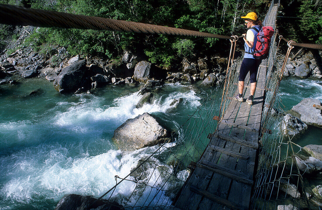 Hiker on suspension bridge crossing Inn, Unterengadin, Grisons, Switzerland
