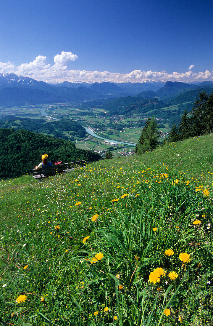 Hiker sitting on a bench at Kranzhorn with a view over the Inn valley, Kaiser Mountain Range and Central Eastern Alps, Chiemgau Alps, Tyrol, Austria