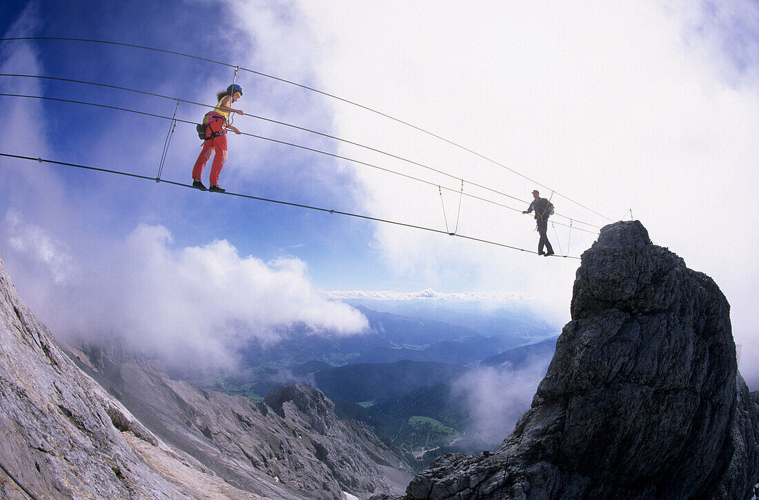 Two mountaineers meeting halfway on a rope bridge, Koppenkarstein west ridge, Dachstein range, Upper Austria, Austria