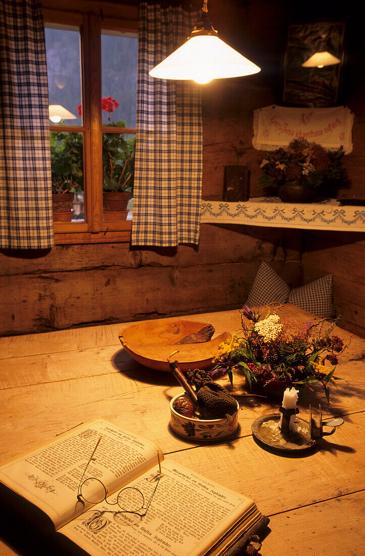 Stube in einem alten Bauernhaus mit aufgeschlagenem Buch und Lesebrille auf dem Tisch, Gosau, Oberösterreich, Österreich