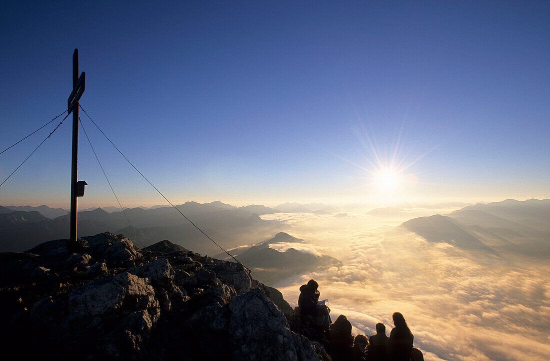 A group of people at a cross at the summit of Grimming with view over the fogbank of Enns valley towards Gesaeuse, Dachstein range, Styria, Austria