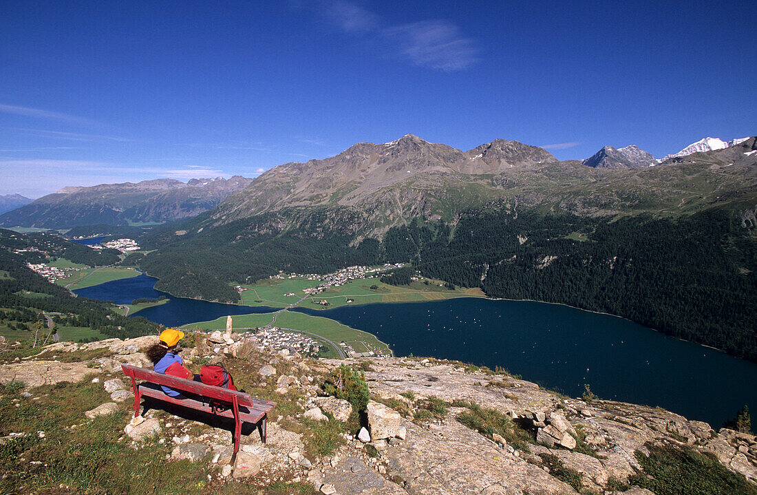 Hiker resting on a red bench with views to the Engadin lakes, St. Moritz and Bernina Mountain range, Upper Engadin, Grisons, Switzerland