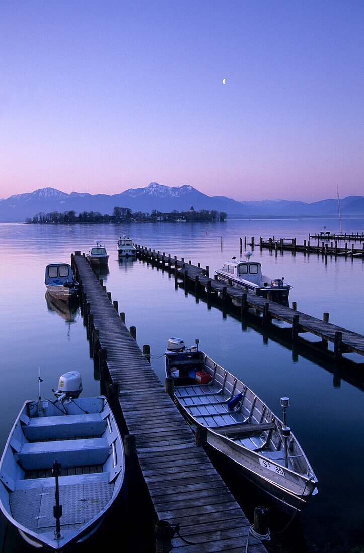 Landing stage and boats in Gstadt at lake Chiemsee at dawn with Fraueninsel, Hochgern and Hochfelln in the background, Chiemgau, Upper Bavaria, Bavaria, Germany
