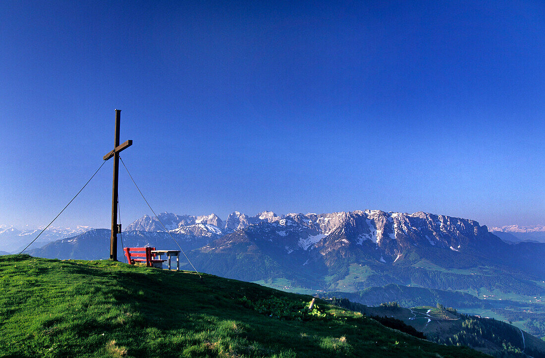 Red bench and cross on the summit of Wandberg with view to Wilder Kaiser and Zahmer Kaiser, Chiemgau alps, Tyrol. Austria