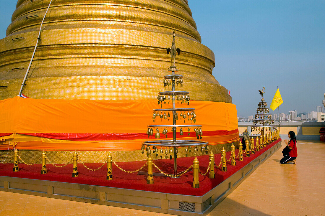 Woman praying in front of gilded Chedi, housed a Buddha relic of the Wat Saket on the Golden Mount, Bangkok, Thailand