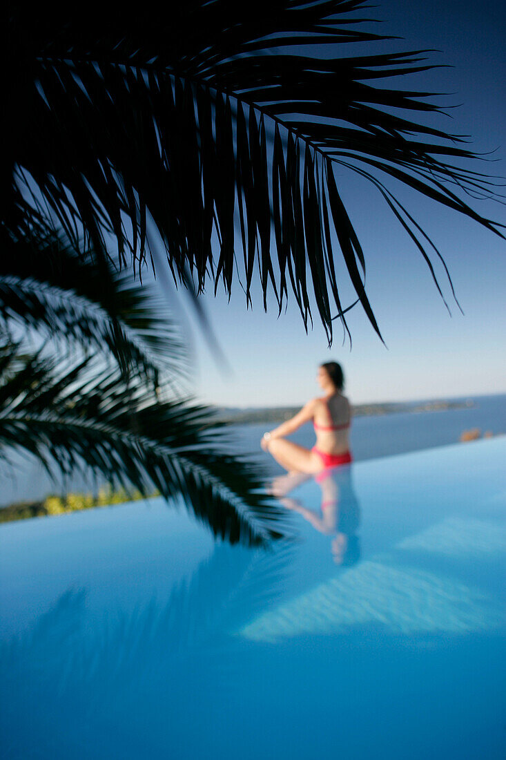 Woman sitting at edge of outdoor pool, sea in back, Bay of Porto Vecchio, Southern Corse, Frankreich