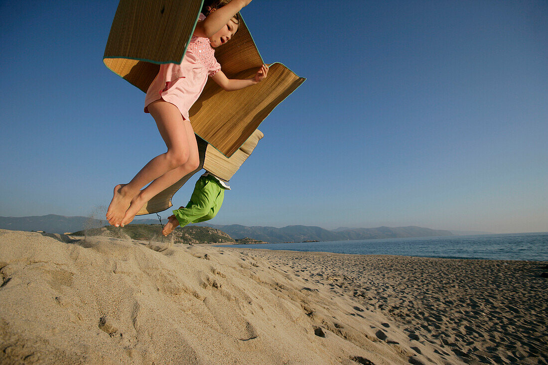 Two children  jumping from dune, Liamone Beach, Western Corse, France