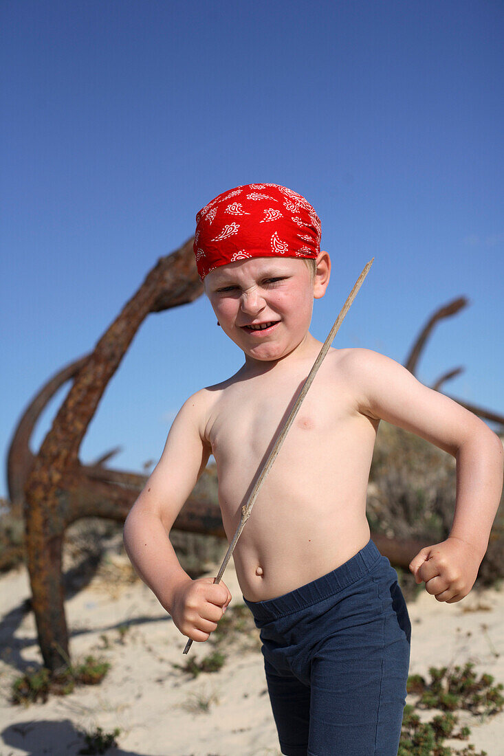 Junge spielt Pirat zwischen rostigen Ankern am Strand, Ilha de Tavira, Tavira, Algarve, Portugal