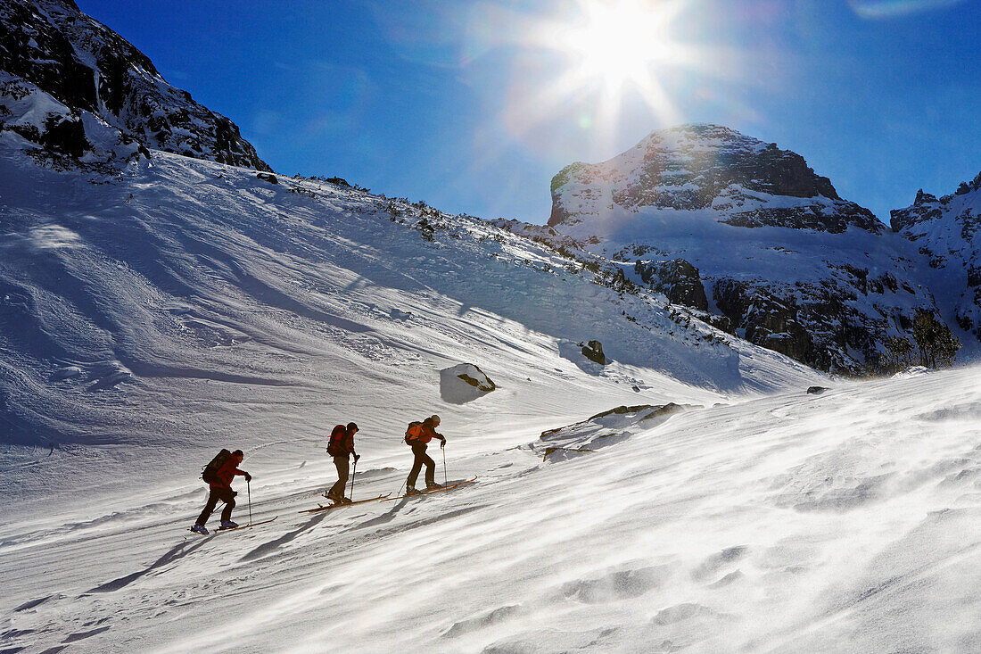Drei Menschen steigen mit Skiern auf zum Gipfel des Maljovica. Der Wind bläst den Schnee über die Oberfläche, Rila Gebirge, Bulgarien, Europa