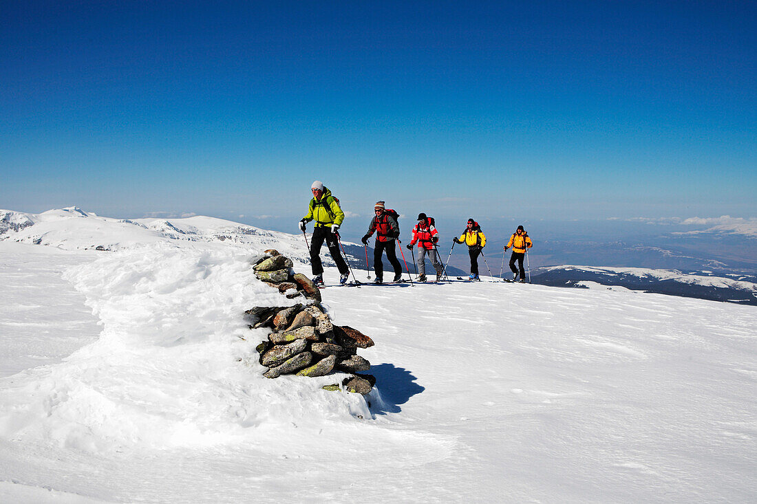 Eine Gruppe Skitouristen steigt auf mit Skiern und Fellen zum Gipfel des Popova Kapa. Den höchsten Punkt ist mit einem Steinmann markiert. Bulgarien, Rila Gebirge, Europa, MR