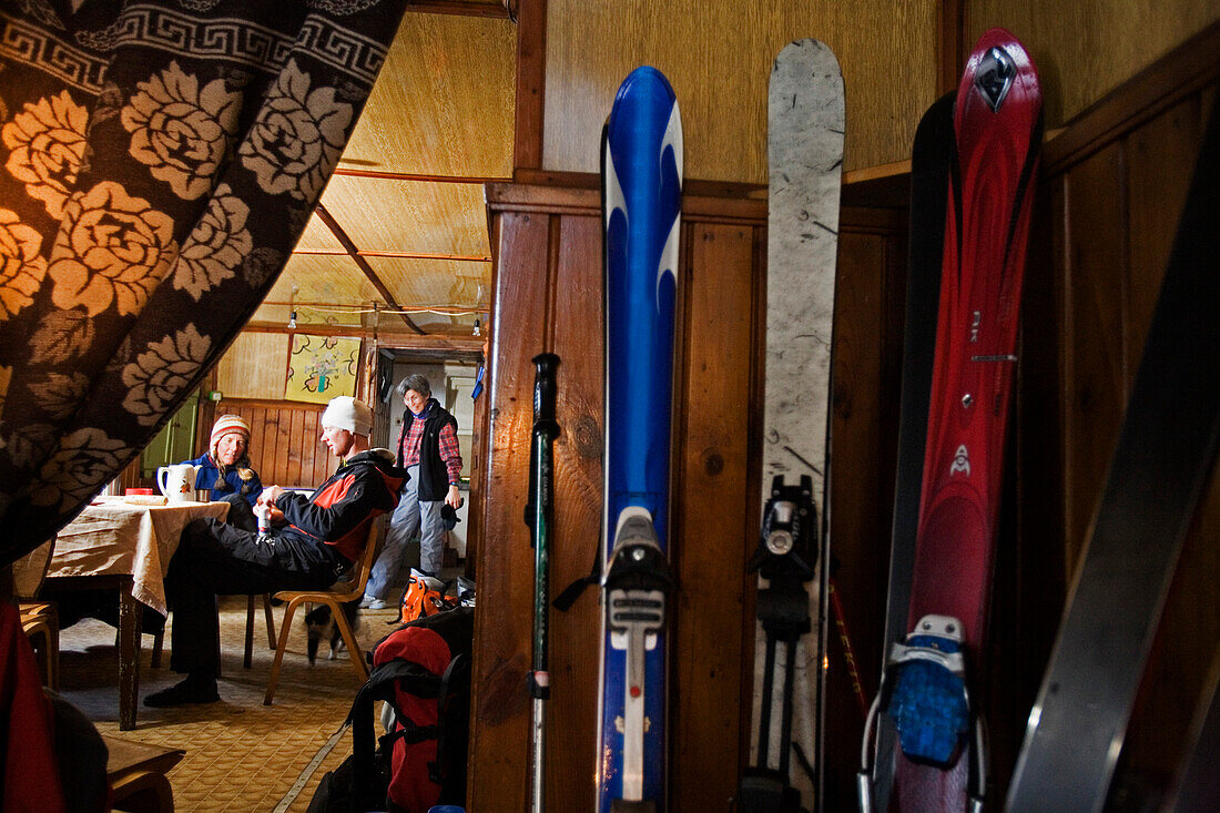 Skis and three people inside the bulgarian Demjanica hut, Pirin Mountains, Bulgaria, Europe