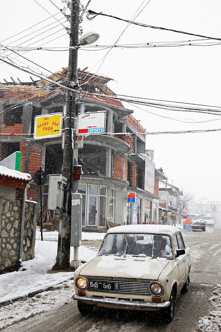 Altes Auto fährt durch Schneematsch im Wintersportort Bansko, Pirin Gebirge, Bulgarien