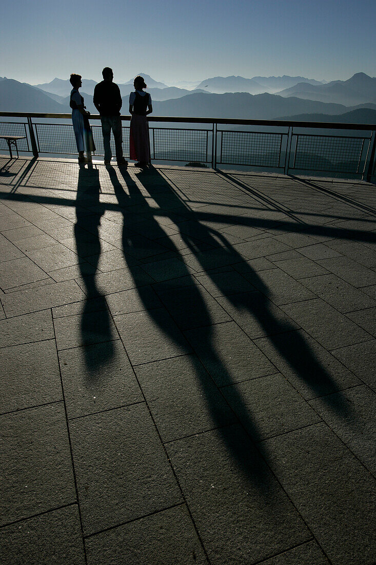 Two waitresses and a waiter standing on the terrace of Brauneckhaus watching the morning sun rise, Brauneck, Bavaria, Germany